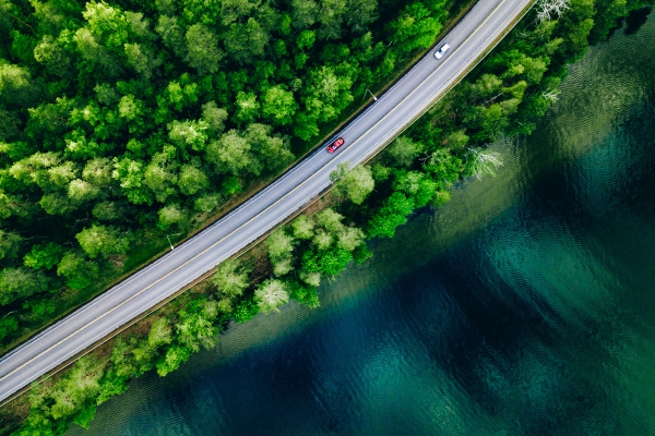 Red and white car on road next to green forest and water