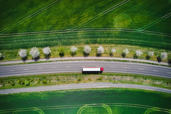 Red and white truck driving on road next to green grass